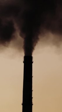 Siyah yoğun duman endüstriyel borulardan geliyor. Kimyasal duman akşam gökyüzünün atmosferini kirletir. Yakın plan. Dikey video