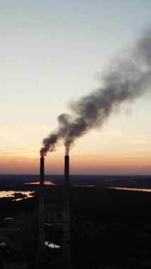 Ekolojik felaket. Akşamları endüstriyel borulardan gelen kirli emisyonlar doğal çevreye yayılıyor. Gün batımında nehrin yanındaki fabrikada. Dikey video
