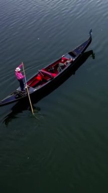 Gondol suda yüzüyor. Gün batımında mavi nehirde bir teknede dinlenen güzel bir kadın. Üst hava manzarası. Dikey video