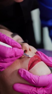 Güzellik uzmanı, kadının dudaklarının dış hatlarını boyar. Dudaklardaki kalıcı makyajdan önce hazırlık. Plastik tıp ve kozmetoloji. Dikey video