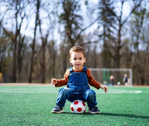 Menino Está Sentado Grama Com Uma Bola Futebol Frente Dele Fotos De Bancos De Imagens