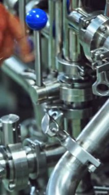 Modern bir fabrikada otomatik makineyi çalıştıran işçiler. Bir mandıra fabrikasında modernize edilmiş bir makinenin çalışmasını başlatmak için metal aletleri çalıştıran bir işçi. Yakın plan. Dikey video