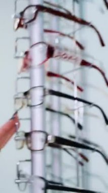 Gözlük dükkanı. Optik mağazasında gözlüklü dur. Kadın eli bardakları seçer. Dikey video