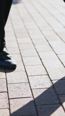 Sokakta dans eden siyah ayakkabılı adamın bacakları için yakın plan. Siyah ayakkabılı ve pantolonlu bir erkek, kaldırımda mutlu bir şekilde dans eder. Dikey video