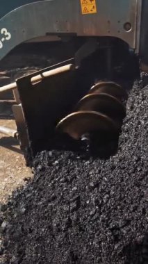 Yola sıcak asfalt döken ağır bir kaldırım makinesinin metal yapısı. Asfalt ayırıcı çalışıyor. Büyük bir kamyon siyah ziftlenmiş. Yakın plan. Dikey video