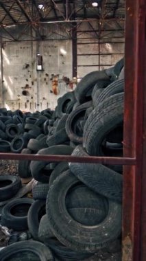 Terk edilmiş bir fabrikada bir sürü araba lastiği var. İçerideki eski fabrikanın manzarası. Yakın plan. Dikey video