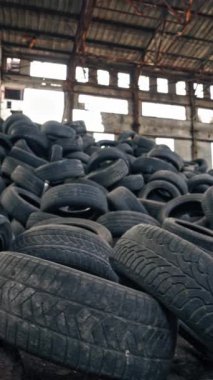 Eski terk edilmiş binanın zemininde duran siyah çöp lastikleri. Farklı araçlardan alınan pek çok kullanılmış lastik lastik içerideki ıssız bir fabrikada. Dikey video