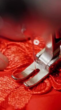 Kırmızı kumaş dikme işlemi güzel bir çiçekle tasarım yapıyor. Dikiş makinesi üzerinde çalışırken terzinin elleri malzeme tutuyor. Yakın plan. Dikey video