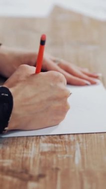 Terzi, modern bir iç mekandaki giysinin yaratıcı bir tasarımını çiziyor. Ahşap masada elinde kalem olan genç bir terzinin elleri. Kadınsı bir hobi. Dikey video