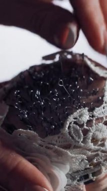 Güzel tırnakları olan, beyaz iğneli iğneden iğne yiyen kadın eli. Tahta masadaki terzi için süngerde bir sürü dikiş iğnesi var. Yakın plan. Dikey video