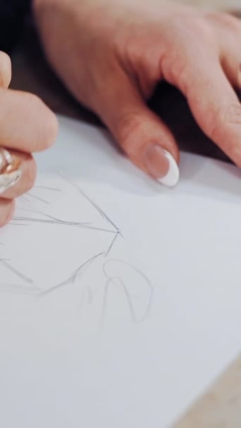 アトリエで服のスケッチを描いたファッションデザイナーの若い女性の手 女性のテーラーは屋内で鋭い鉛筆で描かれています クローズアップ 垂直ビデオ — ストック動画