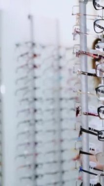 Sağlık hizmeti, görme ve görme konsepti. Optik mağazasında gözlük seçen mutlu kadın. Gözlük dükkanı. Dikey video