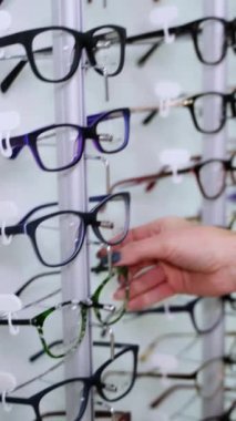 Kürsüde gözlük seçen bir kadın eli. Kadın optik mağazasında yeni gözlük alıyor. Dikey video