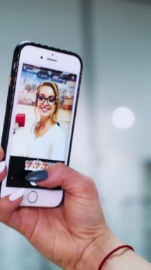 Kadın cep telefonunda kendine bakıyor. Kadının el ele tutuşması ve gözlüklü güzel bir kadınla videoyu göstermesi. Dikey video