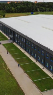 Modern iki katlı bir binanın cephesi. Açık hava sanayi tesisi. Otoparkı olan güzel imalattan oluşan hava manzarası. Yaz zamanı. Dikey video