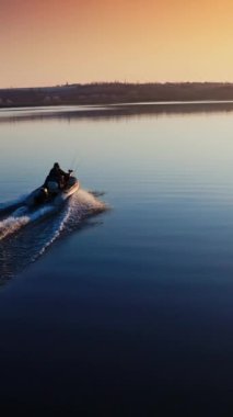 Gün batımında su yüzeyinde tekne. İnsanlar güzel su arka planında akşam nehri boyunca sürat teknesini sürüyorlar. Hava görüntüsü. Dikey video