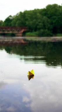 Akşamları nehirde el yapımı sarı ve mavi kağıt gemiler yüzüyor. İki origami teknesi sakin bir nehirde süzülüyor ve gökten suya az miktarda yağmur yağıyor. Dikey video