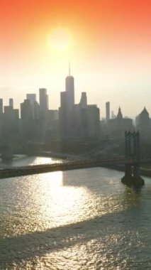 New York gökdelenlerinin gri siluetlerinin üzerine güneş batıyor. Pembe gökyüzünün arka planında Doğu Nehri üzerindeki güzel köprüler. Dikey video