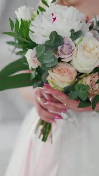 美しい花嫁の手にクリーミーなバラの結婚式の花束 白いウェディングドレスを着た素敵な若い女性が花を持っています クローズアップ バーティカルビデオ — ストック動画