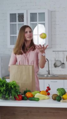 Mutfak masasında sağlıklı yiyecekler. Güzel bir kadın alışveriş çantasından taze elma çıkarıyor. Sevgi dolu anne beslenmeyi önemser. Dikey video
