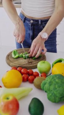 Masanın üzerinde organik sebze ve meyve var. Kadın sağlıklı yemek hazırlamak için ahşap bir tahtada yeşil biber kesiyor. Diyet konsepti. Dikey video