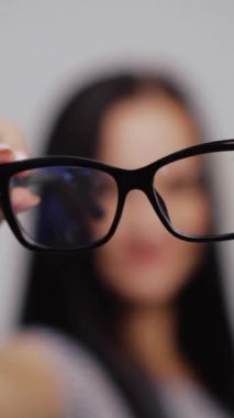 Bir kadının bulanık arka planına yakın plan moda gözlük. Kadın gelir ve siyah çerçeveli yeni gözlük takar. Dikey video