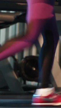 Mor taytlı kadın fitness kulübünde modern bir koşu bandında koşuyor. Spor salonunda spor ayakkabılarla koşan bacaklar. Kardiyo eğitimi. Yakın plan. İnce beden için spor. Dikey video