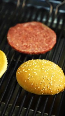 İki hamburger ekmeği ve bir pirzola ızgarada pişiriliyor. Lezzetli ev yapımı burger. Dikey video