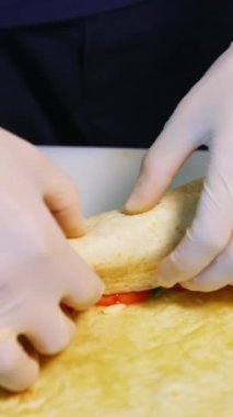 Sebzeli etli ve peynirli pide pişirmek. Lateks eldivenli eller pide rulosunu sarar. Video kavramı. Dikey video