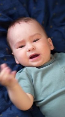 Aktif beyaz erkek bebek çığlık atmak için sırtüstü yatıyor. Sevimli çocuk endişe içinde el ve bacaklarını sallıyor. Üst Manzara. Dikey video