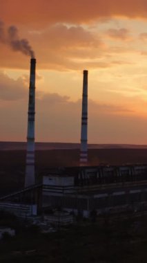 Nehir kıyısında bacası olan endüstriyel rafineri. Endüstriyel bölgede inanılmaz bir gün batımı. Yukarıdan bak. Dron 'un videosu. Dikey video