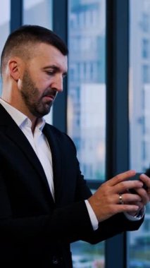 Kendine güvenen iş adamı telefona cevap verir. Takım elbiseli adamın pencerenin yanında kısa bir telefon konuşması var. Dikey video