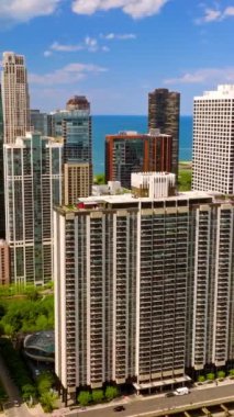 Güneşli bir günde çok katlı binalar ve gökdelenler. Mavi gökyüzü ve mavi göl suyunun arkaplanındaki muhteşem Chicago mimarisi. Dikey video
