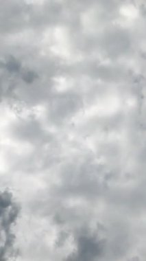Gökyüzünü kaplayan ağır beyaz ve gri bulutlar. Düşük açılı perspektif, hareket eden bulutların zamanlaması. Dikey video