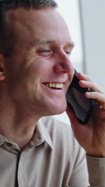 Beyaz, orta yaşlı bir adam telefonda konuşuyor. Ofiste iş görüşmesi yapan bir adamın portresi. Arkaplan bulanık. Dikey video