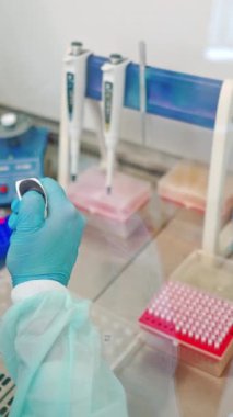 Steril masada deney tüpleri olan tıp bilimcilerinin yakın plan çalışmaları. Laboratuvarda plastik şişelerle çalışan kadın asistanların koruyucu eldivenleri. Dikey video