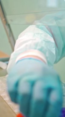 Laboratuvarda çalışan bir işçi. Koruyucu üniformalı laboratuvar teknisyeni klinikteki farklı örneklerle araştırma yapıyor. Yakın plan. Dikey video