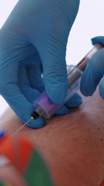 Şırıngaya kan toplamak için adamın kolundaki iğnenin yakın plan görüntüsü. Eldivenli bir tıp çalışanı, damardan kan örneği alıyor. Dikey video
