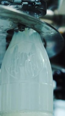 Modern bir gıda fabrikasında süt plastik şişelere dökülüyor. Süt şişelerinin bir süt şirketindeki üretim hattında çekilmiş görüntüleri. Mandıra üretimi yakın plan. Dikey video