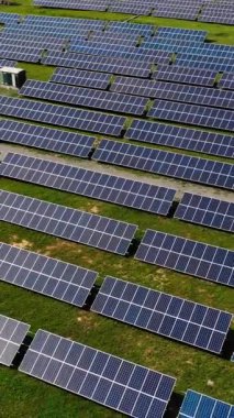 Güneş enerjisi üretim çiftliğindeki güneş panellerinin hava aracı görüntüsü. Sıra sıra dizilmiş mavi güneş panelleri olan büyük bir bölge. Dikey video
