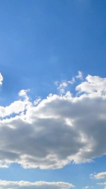 Parlak güneşli açık mavi bir gökyüzü. Açık beyaz bulutlar Güneş 'i bir anlığına biriktirip kaplıyor. Zaman ayarlı. Dikey video