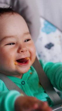 Bebek koltuğunda oturan komik çocuk kaşıkla besleniyor. Childs el sallıyor ve gülümsüyor. Kapatın. Dikey video