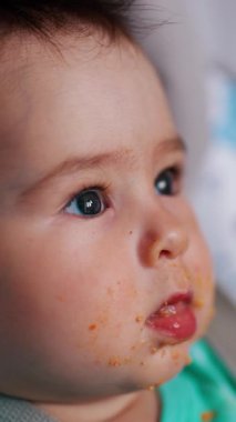 Beslendikten sonra besinle kirletilmiş beyaz bir bebek. Küçük çocuk kaşığı ağzına sokuyor. Kapatın. Dikey video