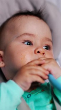 Sallanan sandalyedeki tatlı çocuk kaşığı çiğniyor. Beslendikten sonra bebek. Kapatın. Dikey video