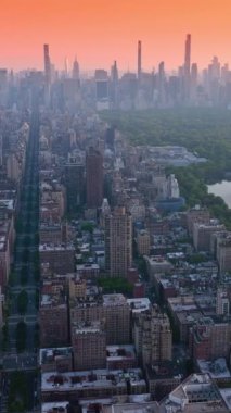 Günbatımında New York 'un engin manzarası. Şehir merkezinde göleti olan bir park yeri. Metropolis, pembe gökyüzünün arka planında. Dikey video