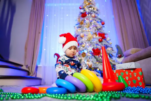 stock image A baby is playing with a set of colorful rings on the floor in front of a Christmas tree