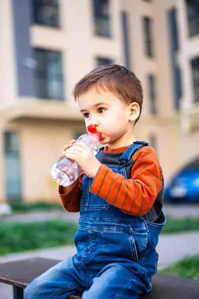 Young Boy Sitting Bench Drinking Water Boy Wearing Blue Overalls Fotografie de stoc