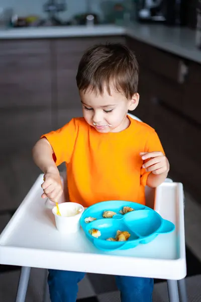 Young Boy Sitting High Chair Eating Food Wearing Orange Shirt Imagini stoc fără drepturi de autor