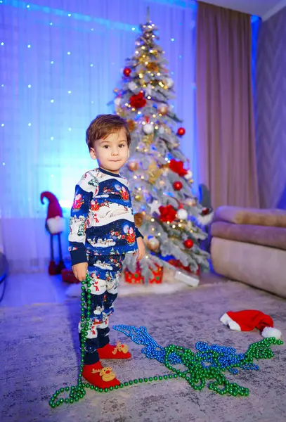 Ung Dreng Står Foran Juletræ Med Julemandstøj Han Holder Perlekæde Stock-foto