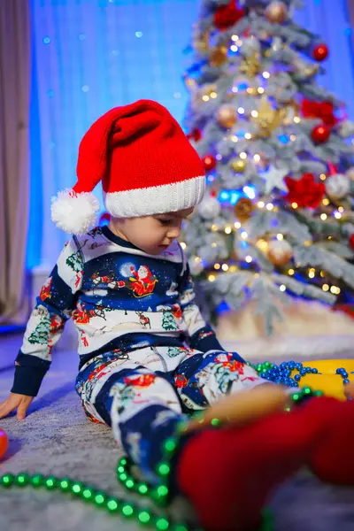 Lille Barn Sidder Gulvet Foran Juletræ Barnet Har Julemandshat Julemandstøj Royaltyfrie stock-billeder